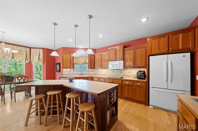 kitchen with white appliances, a sink, light wood-style floors, brown cabinetry, and recessed lighting