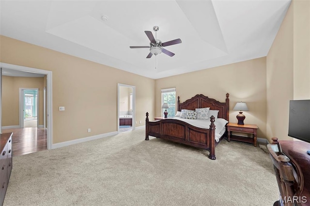 carpeted bedroom with a raised ceiling, multiple windows, baseboards, and ensuite bathroom