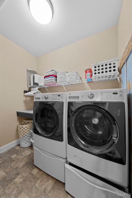 washroom featuring washing machine and dryer, baseboards, and light stone finish flooring