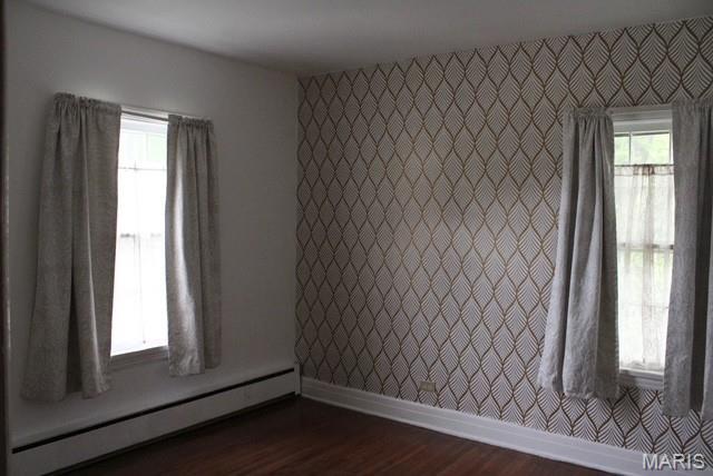 spare room with a baseboard radiator, baseboards, and dark wood-style flooring