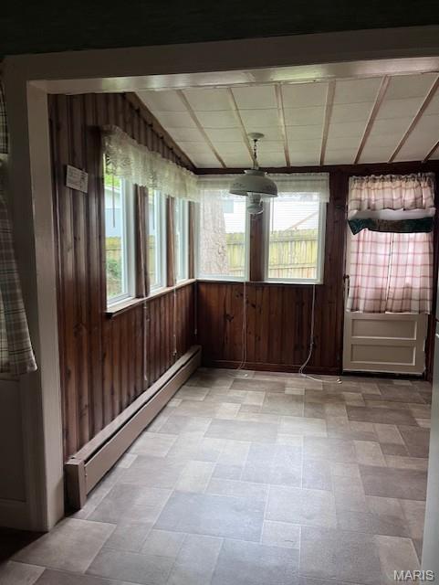 unfurnished room featuring baseboard heating, wood walls, light floors, and lofted ceiling