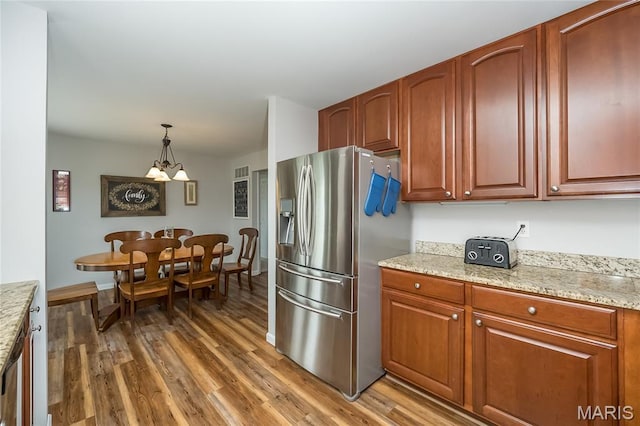 kitchen with stainless steel refrigerator with ice dispenser, light wood-style flooring, hanging light fixtures, and light stone counters