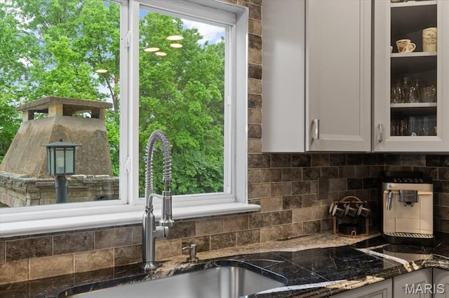 kitchen featuring a sink, tasteful backsplash, white cabinetry, glass insert cabinets, and dark stone counters