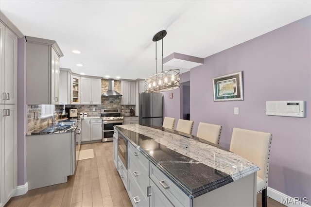 kitchen with appliances with stainless steel finishes, wall chimney exhaust hood, a kitchen island, tasteful backsplash, and light wood-style floors