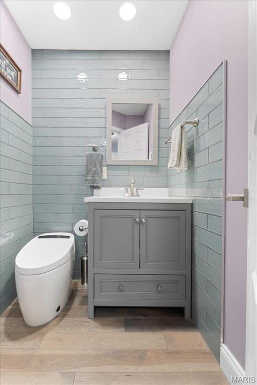 half bath with tile walls, wood finished floors, toilet, and vanity