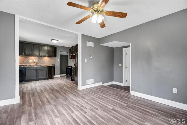 unfurnished living room with wood finished floors, a sink, a ceiling fan, and baseboards