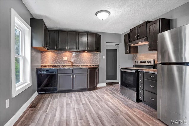 kitchen with stainless steel appliances, under cabinet range hood, plenty of natural light, a sink, and a textured ceiling