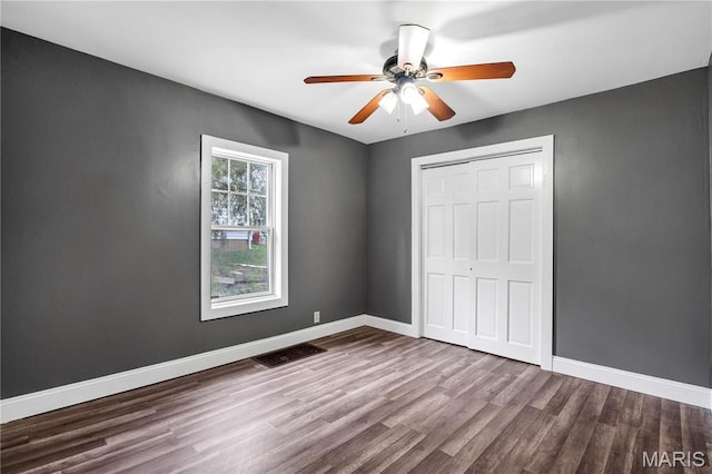 unfurnished bedroom featuring wood finished floors, a closet, baseboards, and ceiling fan