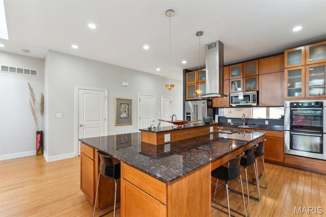 4349 Washington Blvd, Saint Louis, MO 63108 - kitchen featuring appliances with stainless steel finishes, island range hood, light wood finished floors, brown cabinets, and recessed lighting