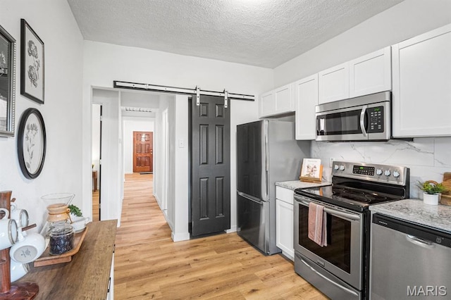 3641 Virginia Ave, Saint Louis, MO 63118 - kitchen with stainless steel appliances, white cabinets, light wood-style floors, decorative backsplash, and a textured ceiling