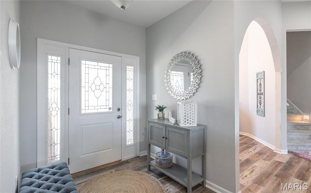 foyer entrance with wood finished floors, baseboards, arched walkways, and stairs