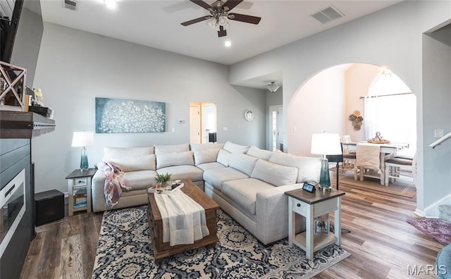 living room featuring a ceiling fan, a glass covered fireplace, wood finished floors, recessed lighting, and arched walkways