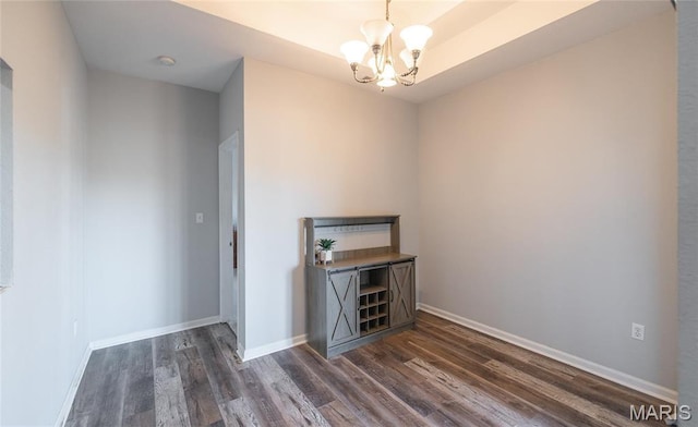 spare room with dark wood-style floors, a chandelier, and baseboards