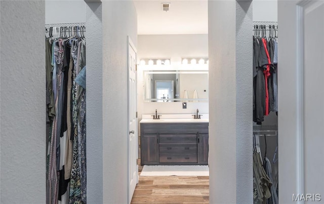 full bath with a textured wall, wood finished floors, double vanity, and a walk in closet