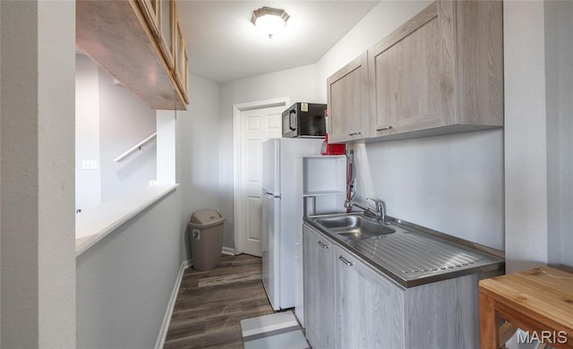 kitchen with a sink, black microwave, dark wood-style flooring, baseboards, and dark countertops