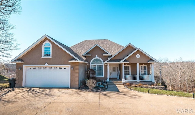 traditional home with concrete driveway, covered porch, a garage, stucco siding, and roof with shingles