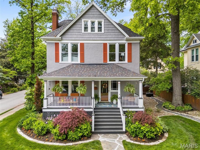 american foursquare style home featuring stucco siding, a chimney, covered porch, stairs, and a shingled roof