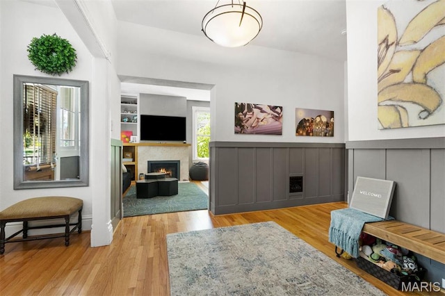 living area with a warm lit fireplace, wood finished floors, wainscoting, and built in features