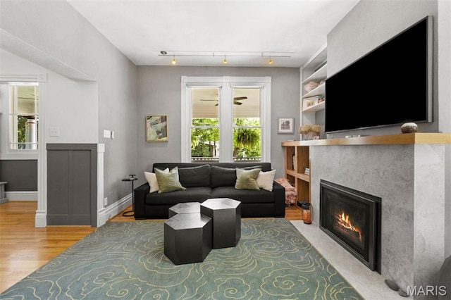 living room with light wood finished floors, healthy amount of natural light, a glass covered fireplace, and track lighting