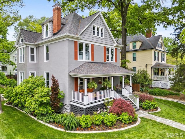 view of front of house with covered porch, stucco siding, a front yard, a chimney, and roof with shingles