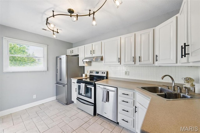 kitchen featuring appliances with stainless steel finishes, under cabinet range hood, a sink, backsplash, and baseboards