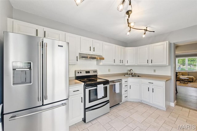 kitchen featuring appliances with stainless steel finishes, under cabinet range hood, a sink, light countertops, and white cabinets