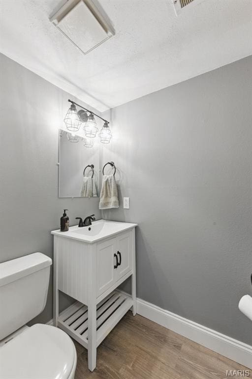 bathroom with wood finished floors, toilet, vanity, and baseboards