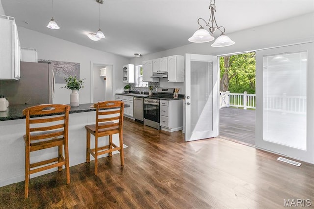 kitchen featuring stainless steel appliances, under cabinet range hood, dark countertops, a peninsula, and vaulted ceiling