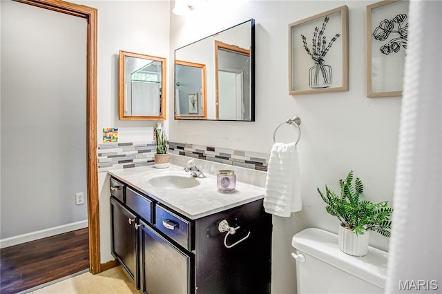 half bathroom with backsplash, toilet, vanity, and baseboards
