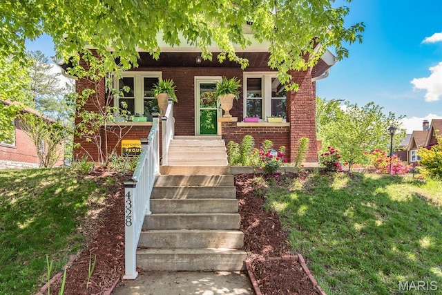 view of front of property featuring brick siding, a front lawn, and a porch