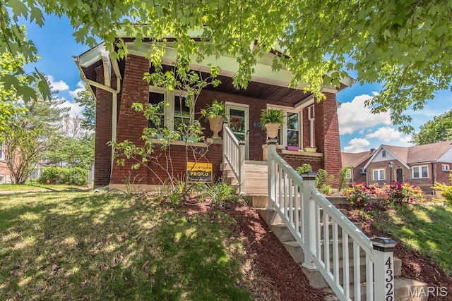view of front facade with covered porch, brick siding, and a front yard