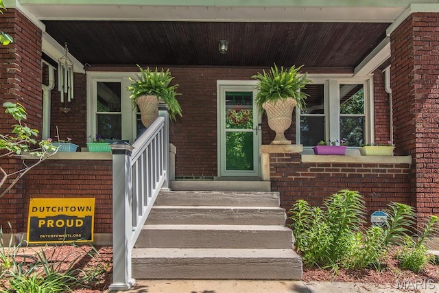 view of exterior entry with a porch and brick siding
