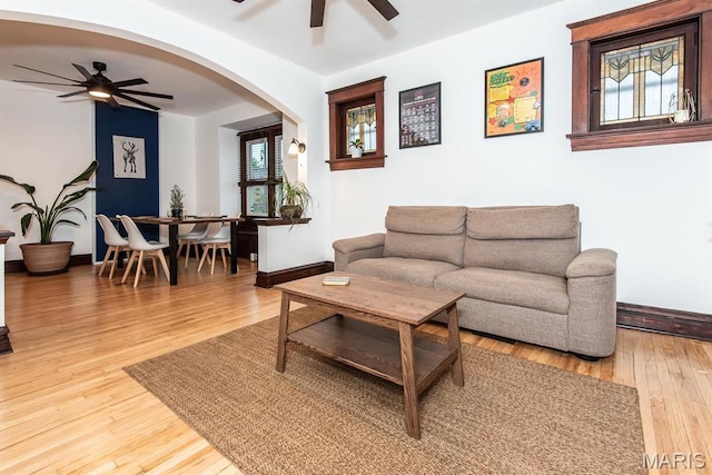 living room featuring a ceiling fan, arched walkways, baseboards, and wood-type flooring