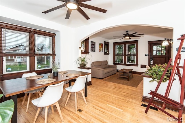 dining room featuring ceiling fan, arched walkways, and light wood-type flooring