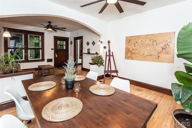 dining area with ceiling fan, arched walkways, wood-type flooring, and baseboards