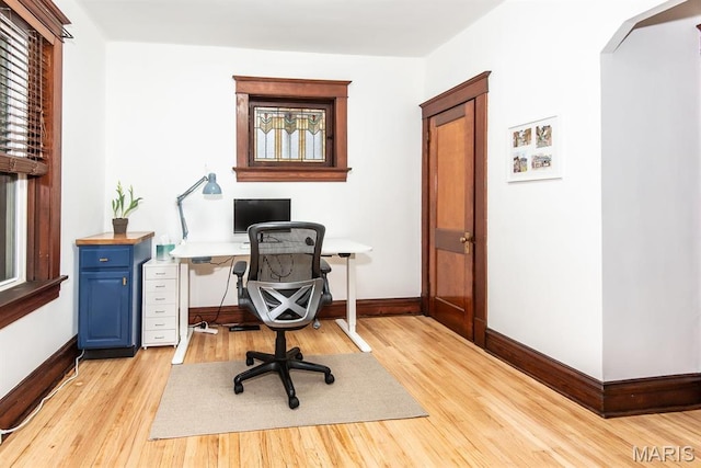 office area featuring arched walkways, light wood finished floors, and baseboards