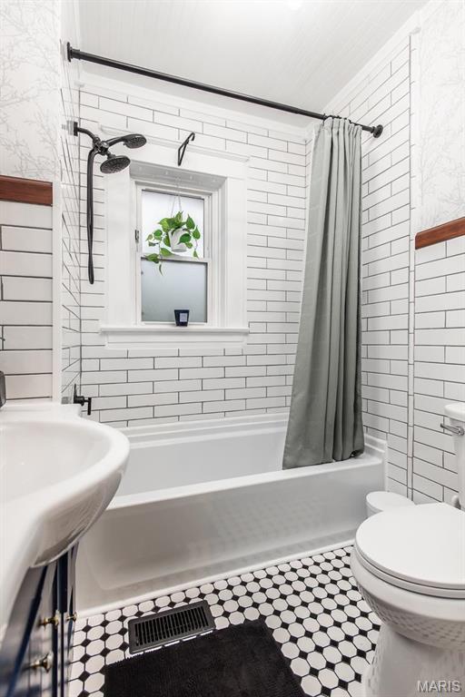 bathroom featuring tile walls, shower / tub combo with curtain, toilet, a sink, and tile patterned flooring