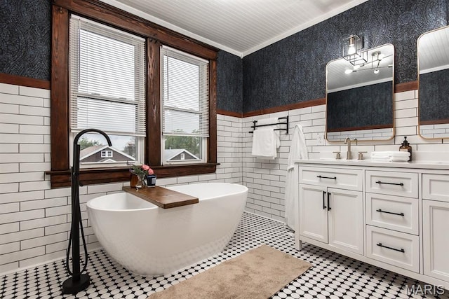 full bath with tile walls, double vanity, a freestanding bath, crown molding, and wainscoting