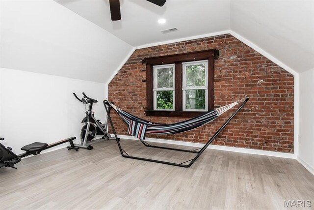 workout area featuring brick wall, vaulted ceiling, wood finished floors, ceiling fan, and baseboards