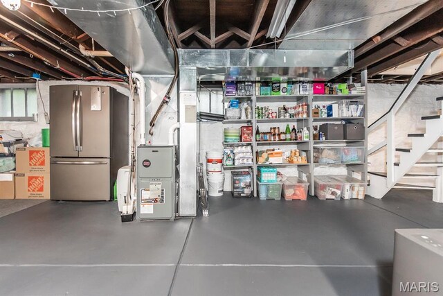 unfinished basement with freestanding refrigerator, heating unit, and stairway