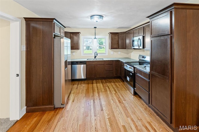kitchen with appliances with stainless steel finishes, light wood-style floors, a sink, and dark brown cabinetry