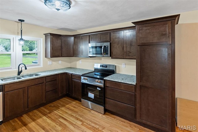 kitchen with appliances with stainless steel finishes, a sink, light wood finished floors, dark brown cabinets, and pendant lighting
