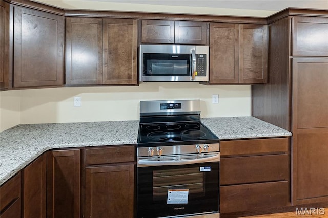 kitchen with stainless steel appliances, dark brown cabinets, and light stone counters