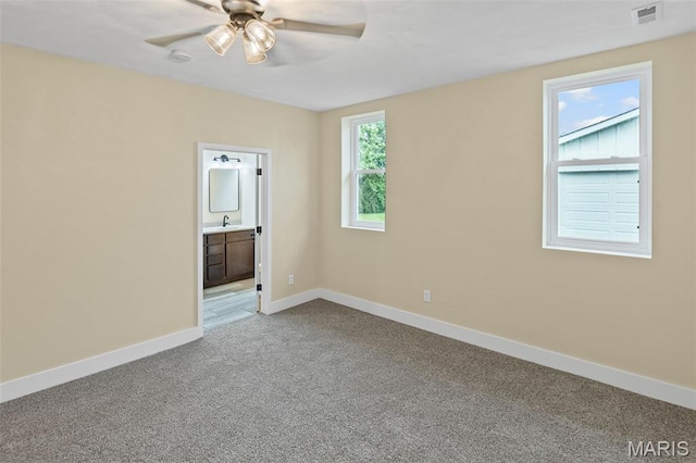carpeted spare room with ceiling fan, baseboards, and a sink