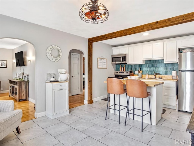 kitchen with stainless steel appliances, arched walkways, a breakfast bar area, and white cabinets