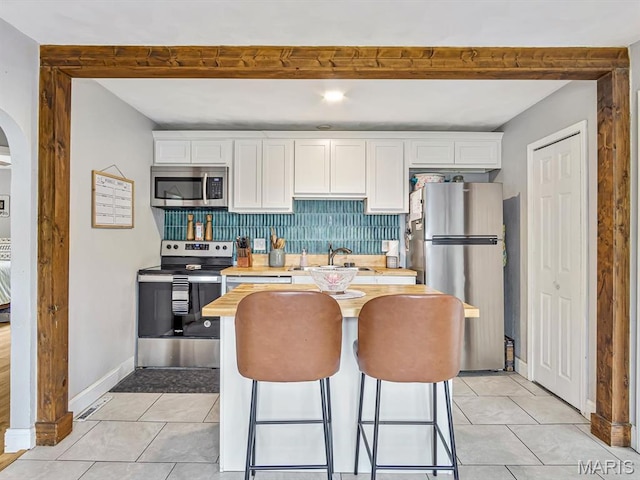 kitchen with appliances with stainless steel finishes, white cabinets, light countertops, decorative backsplash, and beam ceiling