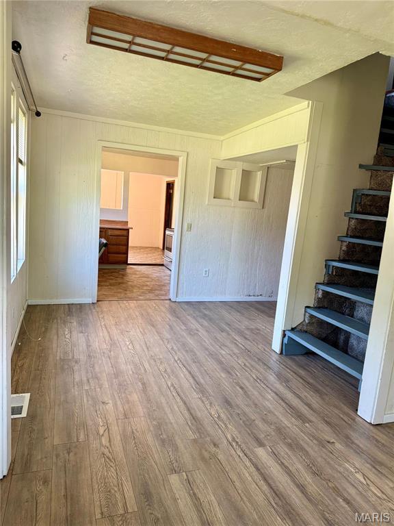 unfurnished living room featuring stairs, wood finished floors, baseboards, crown molding, and a textured ceiling