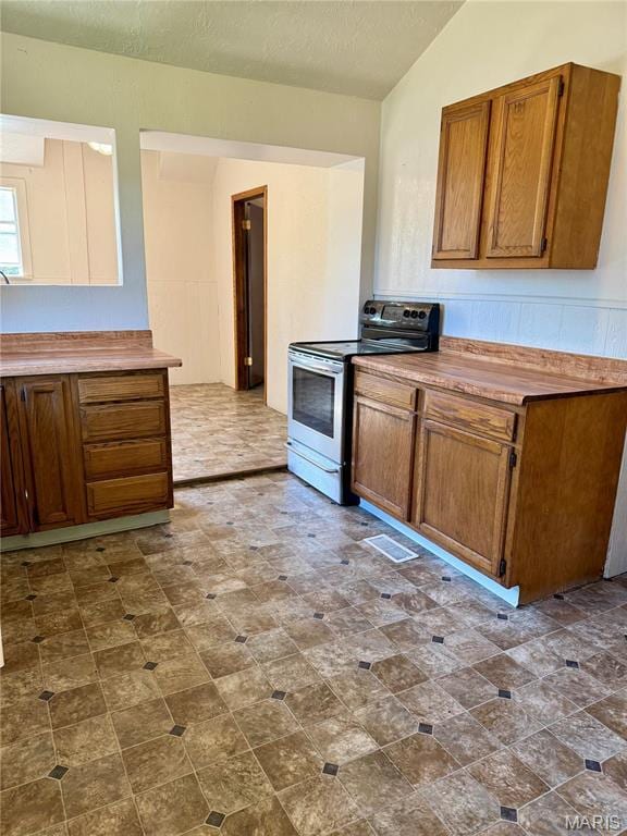 kitchen with stainless steel electric stove, brown cabinets, vaulted ceiling, and a textured ceiling
