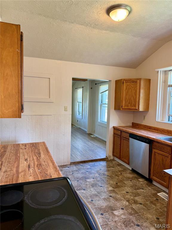 kitchen featuring dishwasher, brown cabinets, vaulted ceiling, a textured ceiling, and black range with electric cooktop