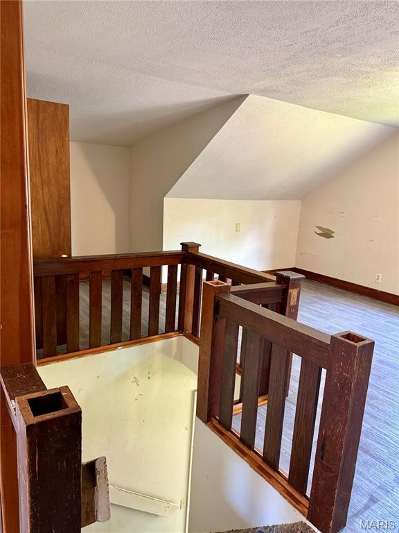 stairway featuring wood finished floors, a textured ceiling, baseboards, and vaulted ceiling